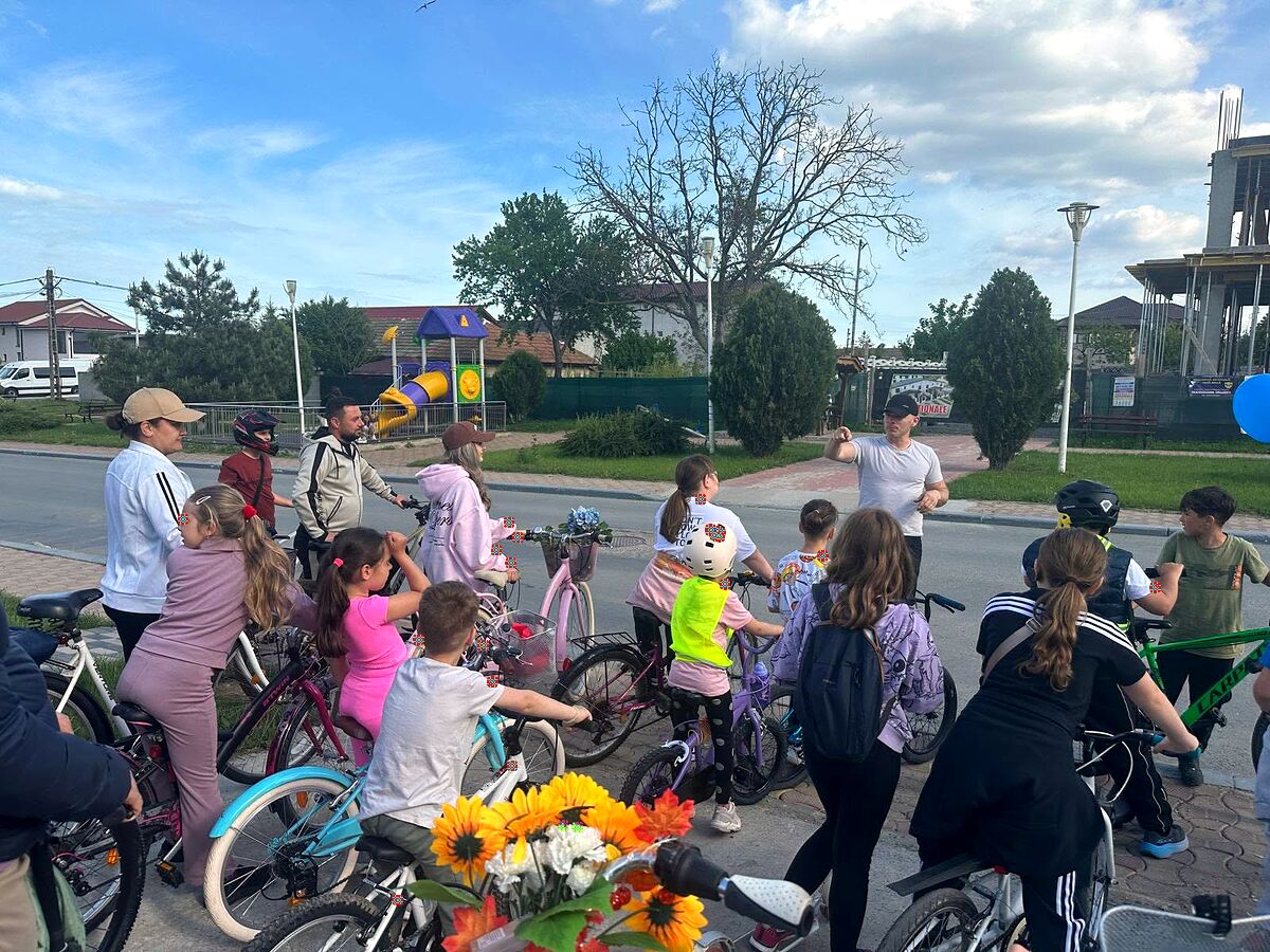 Grup de copii și adulți pe biciclete, adunați în fața brutăriei la plecarea în tură